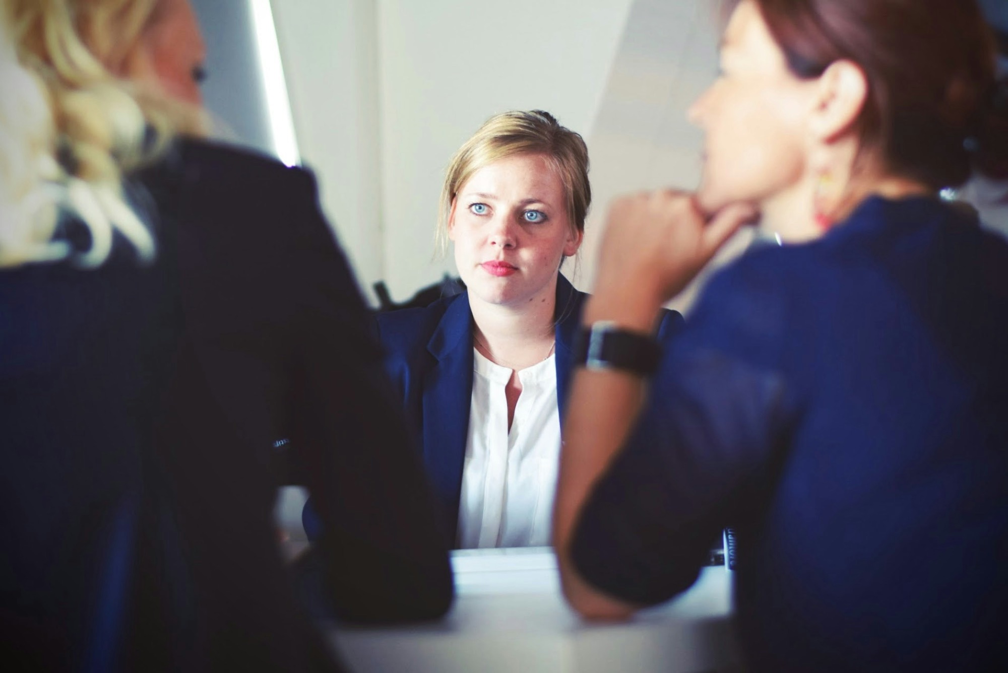 A staff member sits across a table from two colleagues, her expression guarded